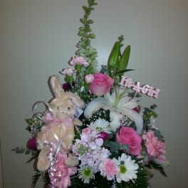 Pink and white floral arrangement with a plush bunny and "It's a Girl" sign