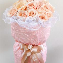 Peach roses arranged in a pink wrapped bouquet with a ribbon and pearl accents
