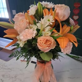 Peach and orange bouquet with lilies, roses, and white daisies in a glass vase