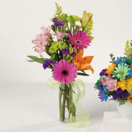 Mixed bouquet of pink, purple, orange, and yellow flowers in a glass vase