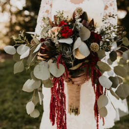 Bride holding a large bouquet with red flowers and trailing greenery