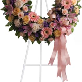 Heart-shaped floral wreath on a stand with pink ribbon
