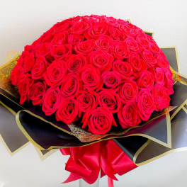 Large bouquet of red roses wrapped in black and gold paper with a red ribbon