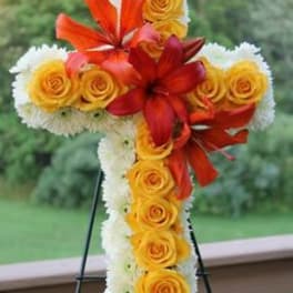 Standing cross-shaped floral spray with yellow roses, white blooms, and orange lilies on an easel