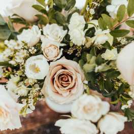 Arrangement of blush roses and white flowers in a white vase on a wooden surface