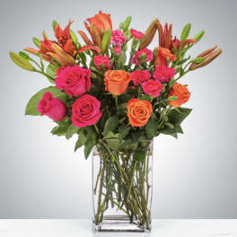 Bouquet of pink and orange roses with lilies in a clear glass vase