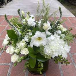 White floral arrangement in a dark glass vase with mixed greenery
