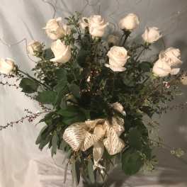 White roses in a clear glass vase with a gold ribbon bow