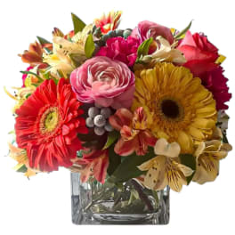 Mixed bouquet of bright gerbera daisies, roses, and alstroemeria in a glass vase