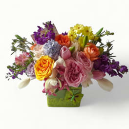 Colorful mixed arrangement of roses, tulips, and other blooms in a green cube vase with a butterfly accent