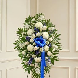 Standing floral spray of white and blue flowers with a blue ribbon