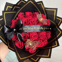 Red roses wrapped in black paper with gold trim and a black ribbon