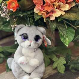 Plush gray cat toy sitting beneath orange and peach flowers