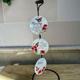Three round memorial plaques hang from a black stand with butterfly and flower designs.
