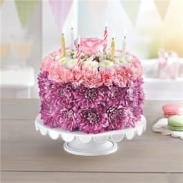 Pink and purple flower-covered cake with birthday candles on a white stand