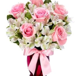 Pink roses and white alstroemeria in a red glass vase with a pink ribbon