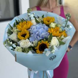 Bouquet of sunflowers, blue hydrangea, and white roses wrapped in pale blue paper