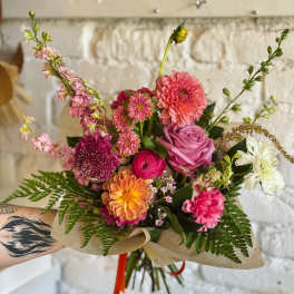 Hand-tied bouquet of pink, orange, and white flowers wrapped in paper