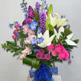 Bouquet of pink roses, white lilies, and blue flowers in a vase with a blue ribbon