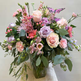 Pink and lavender rose bouquet in a glass vase with a butterfly pick