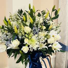 Large white floral arrangement with lilies and roses in a vase with a blue ribbon