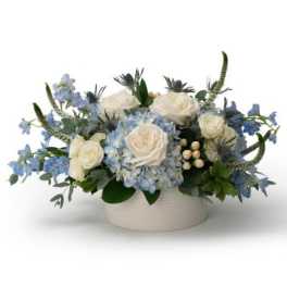 Low arrangement of white roses and blue hydrangeas in a round white ceramic vase