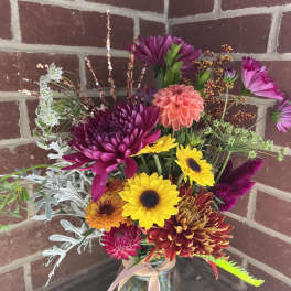 Mixed bouquet of bright chrysanthemums and sunflowers in a glass jar vase
