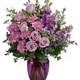 Purple roses and mixed lavender flowers in a purple glass vase