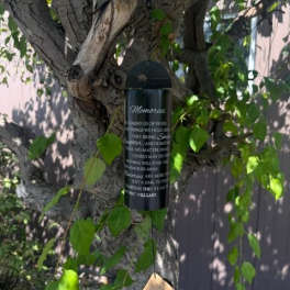 Black memorial wind chime hanging from a tree branch