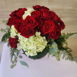 Low round arrangement of red roses and white hydrangeas in a green glass vase