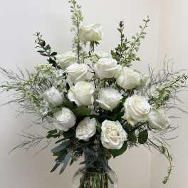 White roses arranged in a clear glass vase with airy greenery