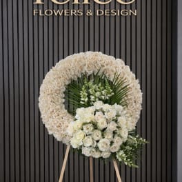 White floral standing wreath on an easel with roses and greenery