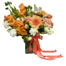 Bouquet of orange and peach flowers in a glass vase with a coral ribbon