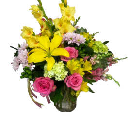 Mixed bouquet of yellow lilies, pink roses, and pale daisies in a glass vase