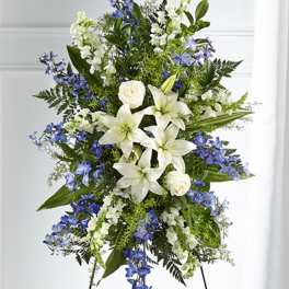 Tall standing spray of white lilies, roses, and blue flowers on a metal easel
