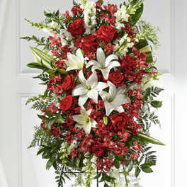 Standing spray of red roses, white lilies, and mixed red and white flowers on an easel.