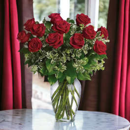 Tall arrangement of red roses in a clear glass vase on a round marble table.