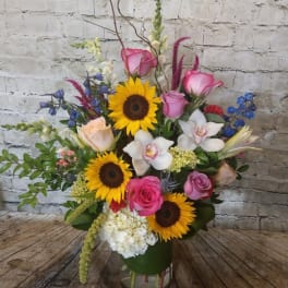 Mixed bouquet with sunflowers, pink roses, and white orchids in a glass vase