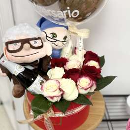 Gift set with red and white roses in a red box, two plush dolls, a bottle, and a clear anniversary balloon.