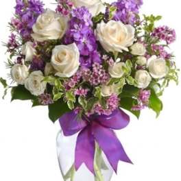 White roses and purple flowers arranged in a clear glass vase with a purple ribbon.