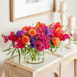 Bright mixed bouquet in a clear glass vase beside two candles