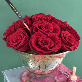 Red roses arranged in a silver pedestal bowl with a black ribbon pick