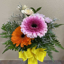 Pink and orange gerbera daisies in a glass vase with a yellow ribbon