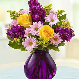 Yellow roses and pink daisies in a purple glass vase