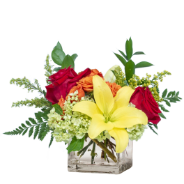 Bouquet of red roses, yellow lilies, and orange flowers in a clear glass vase