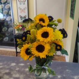 Sunflower bouquet in a glass vase with yellow and dark purple flowers