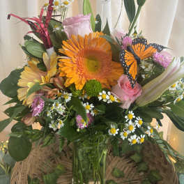 Mixed bouquet with orange gerbera, pink roses, daisies, and a butterfly decoration in a glass vase
