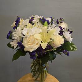 Bouquet of white daisies, cream roses, and purple filler flowers in a glass vase