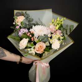 Handheld bouquet of pink and cream flowers wrapped in white paper