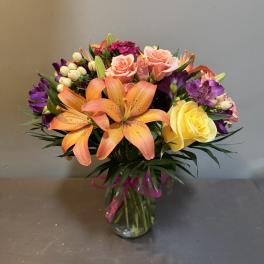 Mixed bouquet of orange lilies, pink and yellow roses in a glass vase